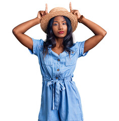 Fototapeta premium Young indian girl wearing summer hat doing funny gesture with finger over head as bull horns