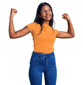 Young indian girl wearing casual clothes and glasses showing arms muscles smiling proud. fitness concept.