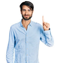 Fototapeta premium Hispanic man with blue eyes wearing business shirt showing and pointing up with finger number one while smiling confident and happy.