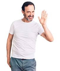 Middle age handsome man wearing casual t-shirt waiving saying hello happy and smiling, friendly welcome gesture