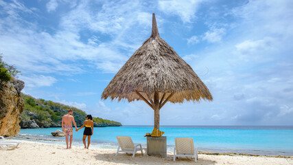 A couple of men and women on vacation in Curacao relaxing at Cas Abao Beach Playa Cas Abao Caribbean island of Curacao, tropical white beach with beach chairs and turqouse colored ocean.