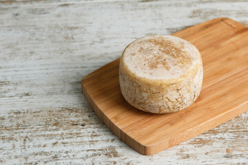 Artisanal and natural whole cheese, placed on a wooden board and without labels.