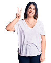 Young beautiful brunette woman wearing casual t-shirt showing and pointing up with fingers number two while smiling confident and happy.