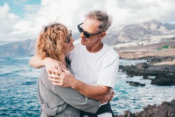 Lovely mature and romantic senior couple embrace each other on the seashore looking into each...