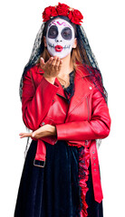 Woman wearing day of the dead costume over background looking at the camera blowing a kiss with hand on air being lovely and sexy. love expression.