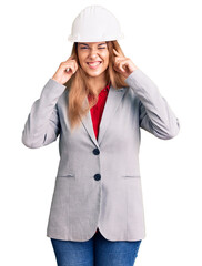Beautiful young woman wearing architect hardhat covering ears with fingers with annoyed expression for the noise of loud music. deaf concept.
