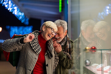 Fototapeta premium Cute senior couple laughing together in front of store window having fun time while shopping.