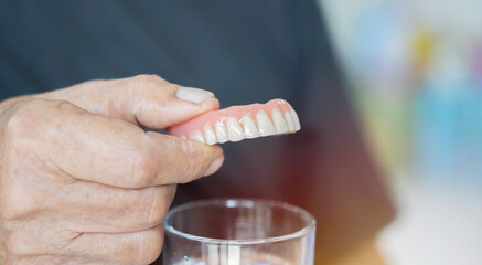 Close up of false teeth in old man hand over the glass. Old age, removable denture concept.