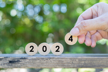 Close up image of hand puting a wooden circle to 2024 over the nature background.