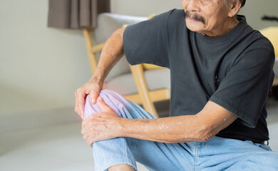 Close up of senior man sitting on floor and suffering from knee ache. - obrazy, fototapety, plakaty