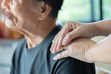 Shot of daughter's hand on older Asian father's shoulder with love and care. Selective focus on...