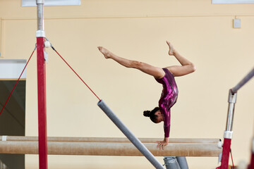 Wide angle shot of brunette female dressed in glossy purple leotard doing single stag handstand on...