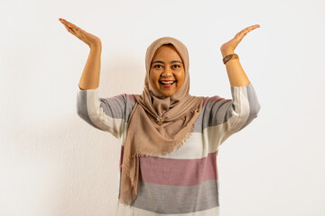 Asian Muslim woman wearing hijab or headscarf, smiling brightly while lifting up her hands....