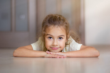 The child lies on the floor in the house, smiles and looks forward. Close-up of a little girl's...