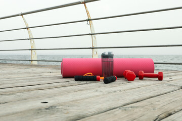 Yoga mat, jump rope, dumbbells and bottle of water on wooden floor outdoors