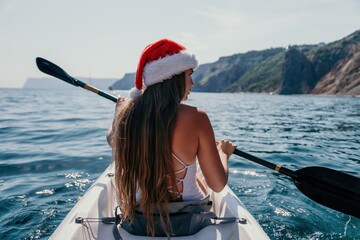 Woman in kayak back view. Happy young woman in Santa hat floating in kayak on calm sea. Summer...