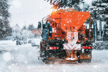 An orange truck with a salt and sand spreader clears the snow and ice from the road. The winter...