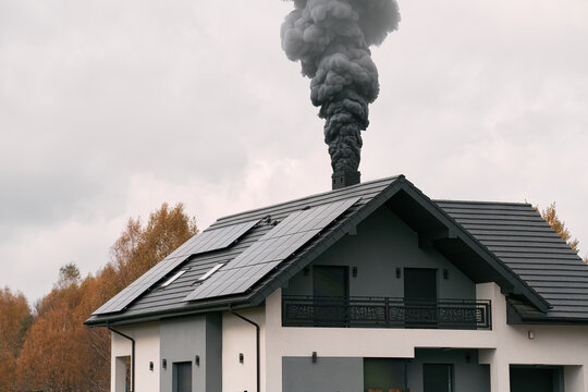 A house with a chimney emits black smoke in the cold air, causing environmental pollution