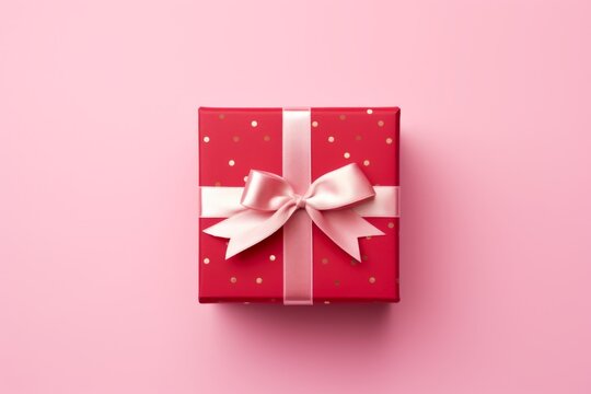 A picture of a red gift box with a pink ribbon and bow on a pink background. Flat lay, top view