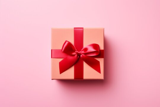 A picture of a peach gift box with a red ribbon and bow on a pink background. Flat lay, top view
