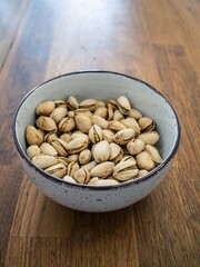 Organic whole pistachio nuts in a white ceramic bowl on wooden table