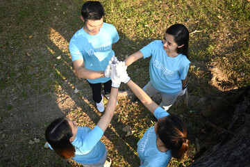 Group of young volunteers stacking hands together showing teamwork spirit. Charity and ecology concept