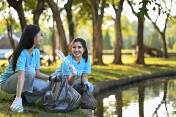 Happy young volunteer women collecting trash in the public park. Environmental protection and charity concept