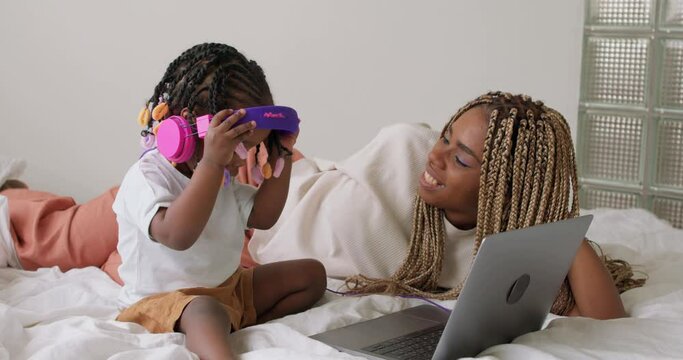 smiling mother putting on headphones while lying on bed with her adorable child, close up slow motion. entertainment lifestyle spare free time