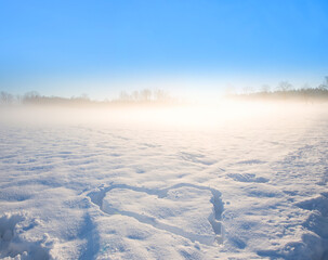 snow covered field with carved love heart, morning fog and blue sky background