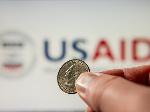 US Quarter Dollar Coin Held in Fingers Against USAID Logo Background