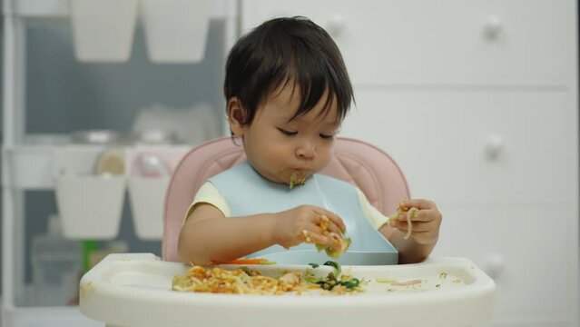 infant baby eating food and vegetable by self feeding BLW or baby led weaning on a chair