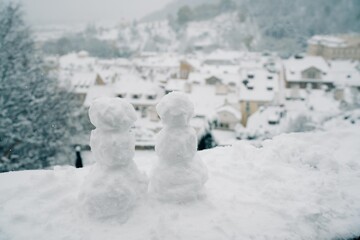 Two snowmen on a background of snowy roofs in Prague