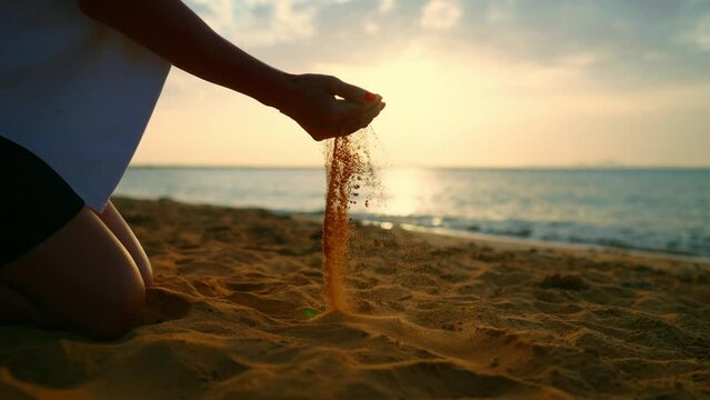 Slow motion shot of hands of an Indian female pouring sand. Sand falling from woman's hand. Close up woman's hands playing with soft sand on the tropical beach at sunrise. Summer holiday at beach.