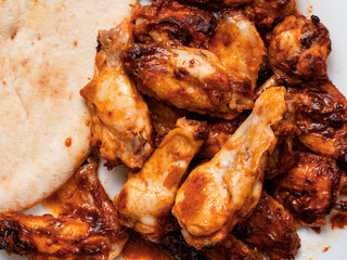 Big portion of barbeque marinated and cooked chicken wings and pitta bread on a white plate. Simple tasty food.