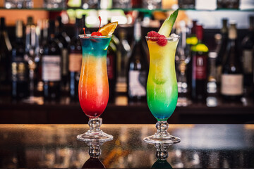 Vibrantly layered tropical cocktails served on a bar, garnished with fruit and berries, with a...