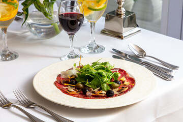 Elegant beef carpaccio with arugula, olives, and shavings of Parmesan, paired with red and white wine, sophisticated table setting for a gourmet experience