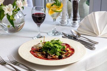 Elegant beef carpaccio with arugula, olives, and shavings of Parmesan, paired with red and white...