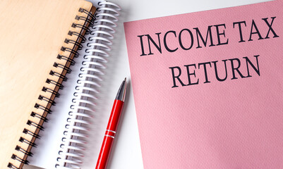 INCOME TAX RETURN word on the pink paper with office tools on white background