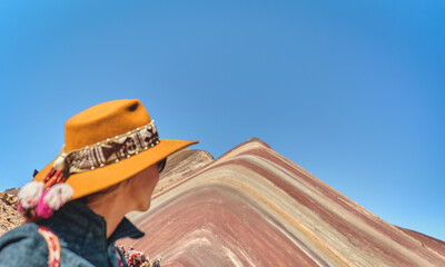 Woman standing in the rainbow mountain in Peru with all the colors of the mountain in the...