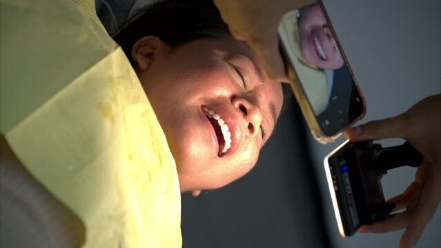 Slow motion vertical shot of a person dentist taking a picture of a latin woman lying down with her mouth open