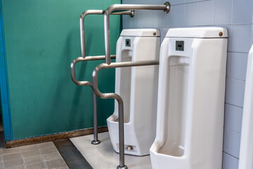 Men's urinals in public restroom with urinal handrails for elder or disabled person.