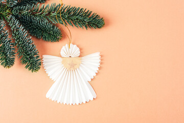 Christmas paper angel hanging on the tree branch on Peach Fuzz color background. Christmas holiday concept. Top view. Trendy color of 2024 Year