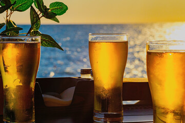 Three transparent glasses of beer stand on table of outdoor cafe by sea at sunset. Beautiful sunset...