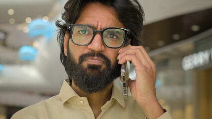 Portrait in office sad Arabian man in glasses talking phone answer business call Close up serious...
