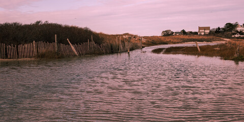 Flooded beach road in Cape Cod coastal village with rustic snow fens and bush hills in the water, Massachusetts, USA