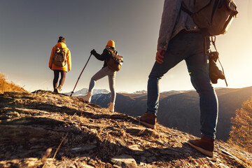 Three young tourists or hikers with backpacks are standing at view point and looking at sunset - obrazy, fototapety, plakaty