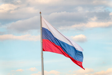 Russian tricolor flag waving in the wind against a blue sky.