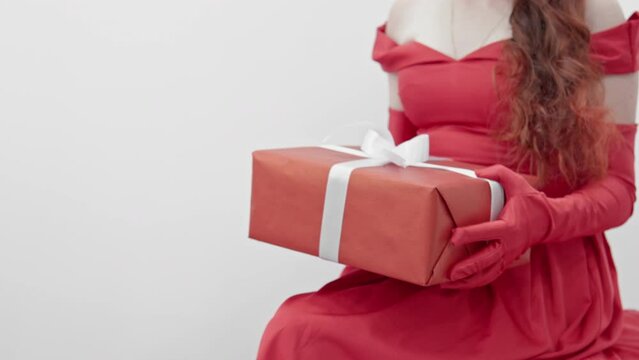A girl in a red dress on a white background holds a gift in a red wrapper and a white ribbon on her lap. A woman admires her gift. Isolated Background