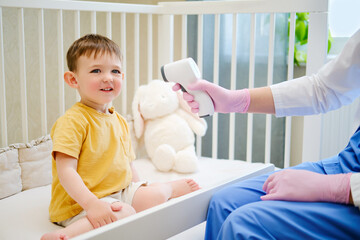 The pediatrician is using a medical thermometer to measure the temperature of the happy baby. Kid aged about two years (one year eleven months)