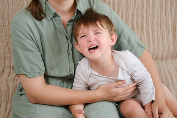 Portrait of an adult woman with a crying baby sitting on a sofa, female age 37 years and male two years